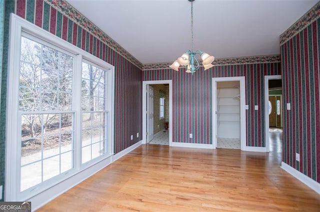 unfurnished dining area featuring a chandelier, wood finished floors, baseboards, and wallpapered walls