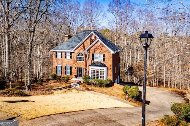 view of front facade featuring driveway, a chimney, and a view of trees