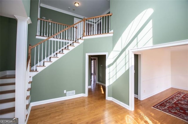 stairway featuring visible vents, wood finished floors, a towering ceiling, and baseboards