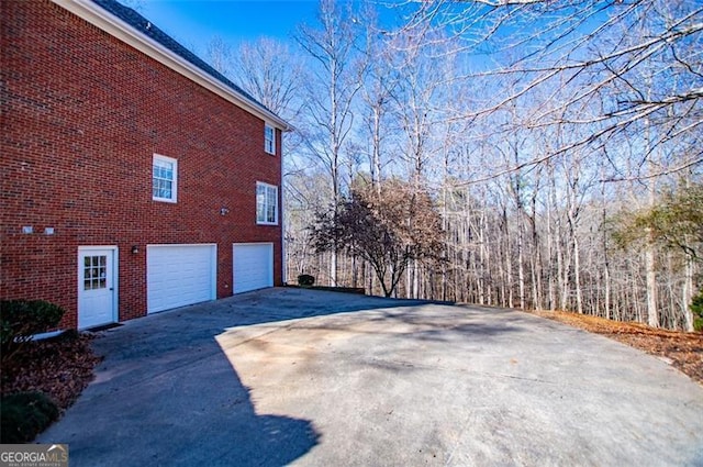 view of property exterior featuring brick siding, driveway, and an attached garage