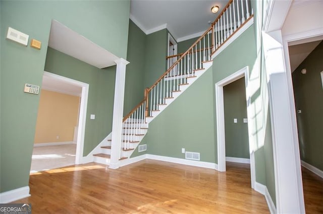 staircase featuring a high ceiling, visible vents, wood finished floors, and ornamental molding