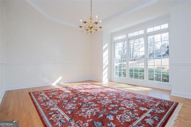 empty room featuring baseboards, crown molding, wood finished floors, and a notable chandelier