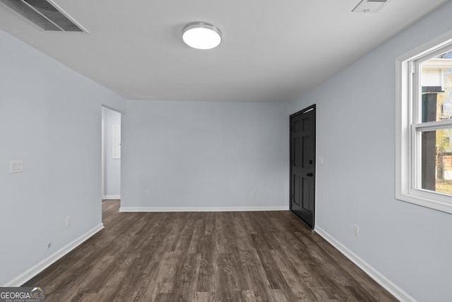 empty room featuring dark wood-style floors, visible vents, and baseboards