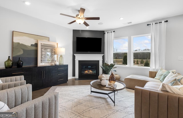 living room with visible vents, a ceiling fan, a glass covered fireplace, wood finished floors, and baseboards