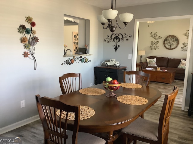 dining space with dark wood-type flooring, a chandelier, and baseboards