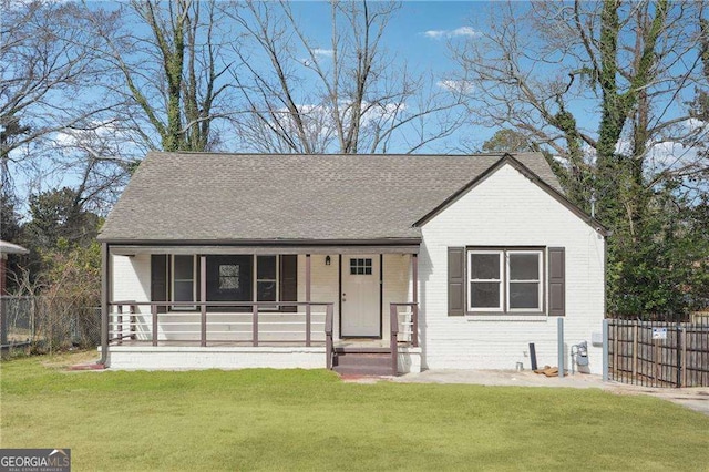 view of front of property featuring covered porch, brick siding, a shingled roof, fence, and a front lawn