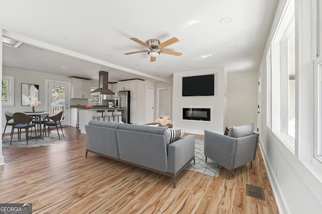 living room featuring a glass covered fireplace, visible vents, light wood-style flooring, and baseboards