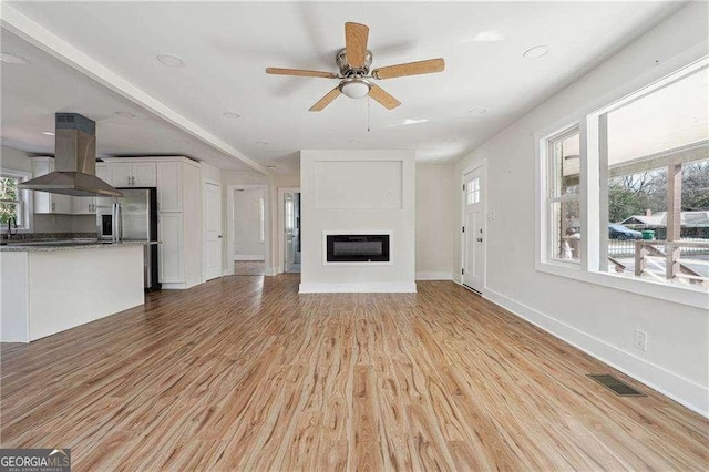 unfurnished living room featuring visible vents, baseboards, a glass covered fireplace, ceiling fan, and light wood-style floors