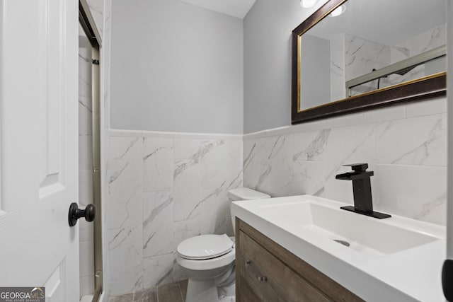 bathroom featuring toilet, a wainscoted wall, tile walls, and vanity