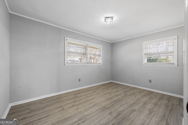 spare room with crown molding, baseboards, and light wood-style floors