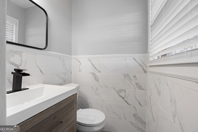 bathroom with toilet, wainscoting, tile walls, and vanity