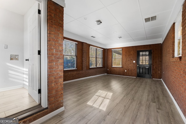 unfurnished living room with light wood-style floors, visible vents, plenty of natural light, and brick wall