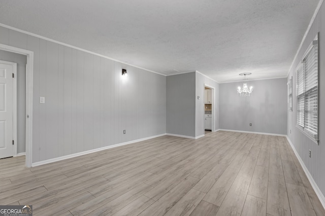 unfurnished living room with a textured ceiling, crown molding, baseboards, light wood-type flooring, and an inviting chandelier