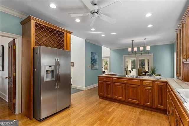 kitchen with ornamental molding, brown cabinetry, tile countertops, and stainless steel fridge with ice dispenser