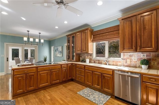 kitchen with tile countertops, stainless steel dishwasher, brown cabinetry, ornamental molding, and a peninsula