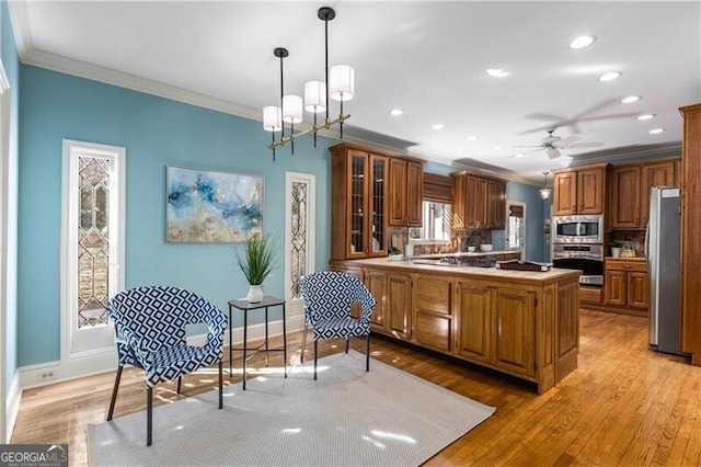 kitchen featuring light wood-type flooring, appliances with stainless steel finishes, brown cabinetry, and ornamental molding