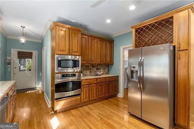 kitchen featuring brown cabinets, tile counters, tasteful backsplash, appliances with stainless steel finishes, and ornamental molding