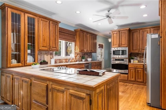 kitchen featuring a peninsula, appliances with stainless steel finishes, backsplash, brown cabinets, and crown molding