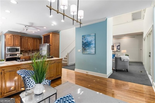 kitchen featuring wood finished floors, ornamental molding, appliances with stainless steel finishes, tile counters, and brown cabinetry