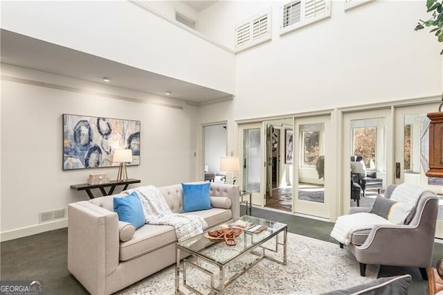 carpeted living room with visible vents, a towering ceiling, and baseboards