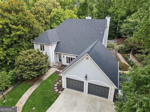 view of front facade featuring an attached garage, a shingled roof, driveway, stucco siding, and a chimney