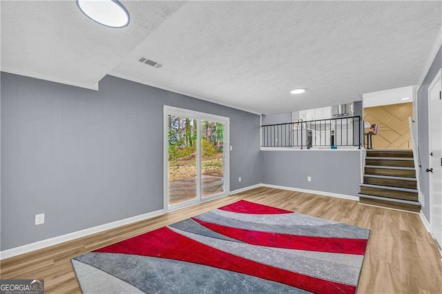 living area with stairs, a textured ceiling, wood finished floors, and baseboards