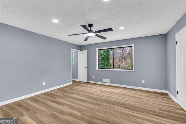 unfurnished room featuring light wood-style floors, baseboards, visible vents, and a textured ceiling