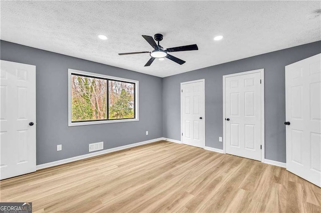 unfurnished bedroom with light wood-style floors, baseboards, visible vents, and multiple closets