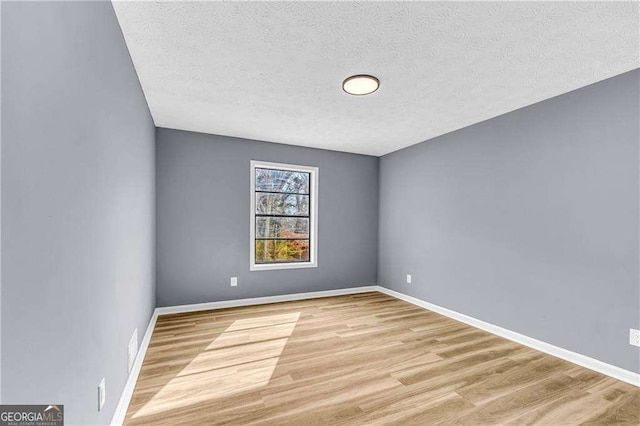 spare room with light wood-style floors, a textured ceiling, and baseboards