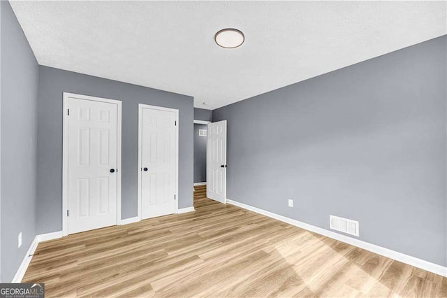 unfurnished bedroom with light wood-type flooring, baseboards, visible vents, and a textured ceiling