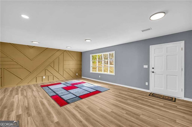 interior space featuring visible vents, an accent wall, baseboards, and wood finished floors