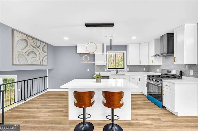 kitchen with wall chimney exhaust hood, stainless steel gas range, light countertops, light wood-type flooring, and a sink