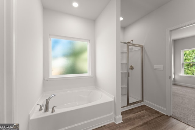 bathroom featuring a shower stall, baseboards, a bath, and wood finished floors