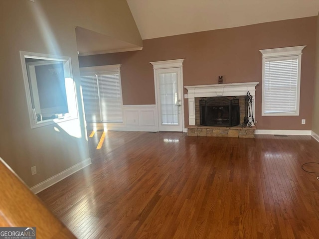 unfurnished living room with a wainscoted wall, a fireplace, vaulted ceiling, wood finished floors, and baseboards