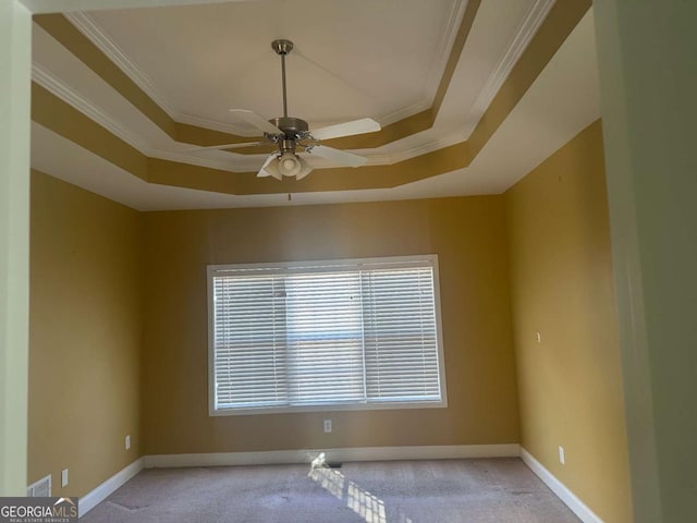 empty room featuring light carpet, baseboards, a ceiling fan, ornamental molding, and a tray ceiling