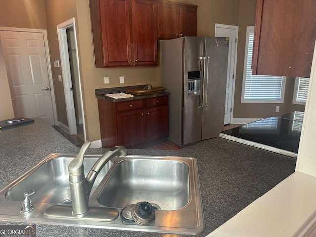 kitchen with dark countertops, a sink, and stainless steel refrigerator with ice dispenser