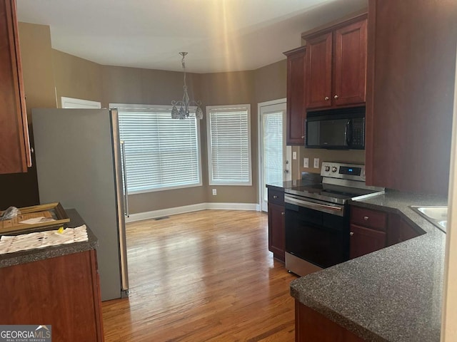 kitchen featuring stainless steel appliances, dark countertops, light wood-type flooring, and an inviting chandelier