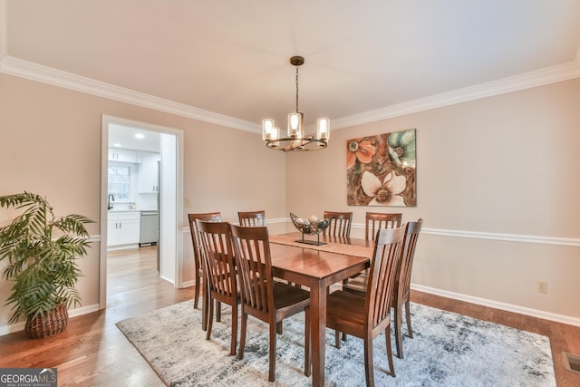 dining room with baseboards, light wood finished floors, crown molding, and an inviting chandelier