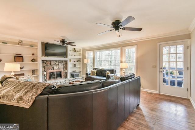 living room with visible vents, baseboards, ornamental molding, a stone fireplace, and light wood-style floors