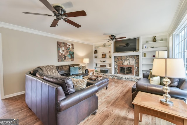 living room with baseboards, ceiling fan, wood finished floors, crown molding, and a stone fireplace