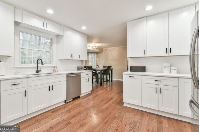 kitchen with light countertops, appliances with stainless steel finishes, white cabinets, a sink, and light wood-type flooring