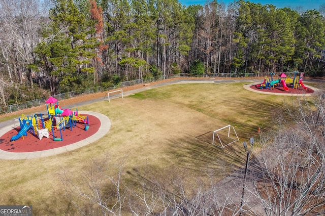 view of yard with playground community, a wooded view, and fence