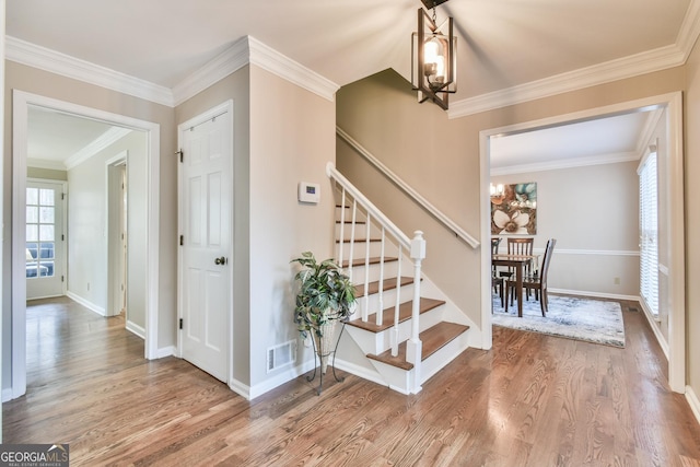 stairway featuring a notable chandelier, wood finished floors, visible vents, baseboards, and ornamental molding