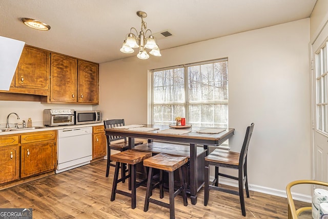 kitchen featuring white dishwasher, a sink, light countertops, brown cabinetry, and stainless steel microwave