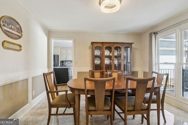 dining area featuring ornamental molding, wainscoting, a decorative wall, and a textured ceiling