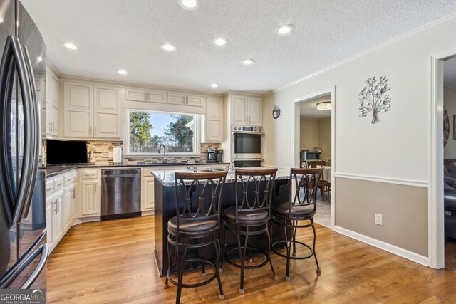 kitchen featuring a sink, a kitchen breakfast bar, ornamental molding, appliances with stainless steel finishes, and tasteful backsplash