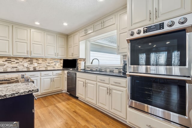 kitchen featuring double oven, dishwashing machine, a sink, light wood-style floors, and tasteful backsplash