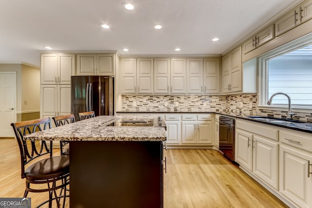 kitchen with black dishwasher, a breakfast bar area, freestanding refrigerator, a sink, and light wood-type flooring