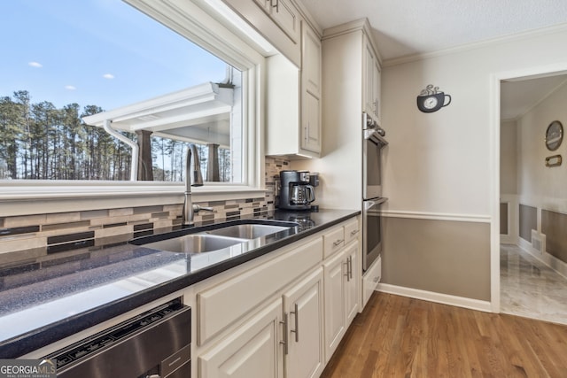 kitchen with wood finished floors, a sink, appliances with stainless steel finishes, decorative backsplash, and crown molding