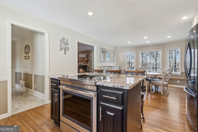 kitchen with light wood-style flooring, a breakfast bar area, stainless steel range with electric cooktop, freestanding refrigerator, and a stone fireplace